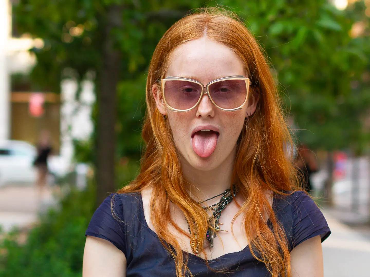 Actor Bobbi Salvör Menuez with red hair wearing sunglasses sticks tongue out playfully.