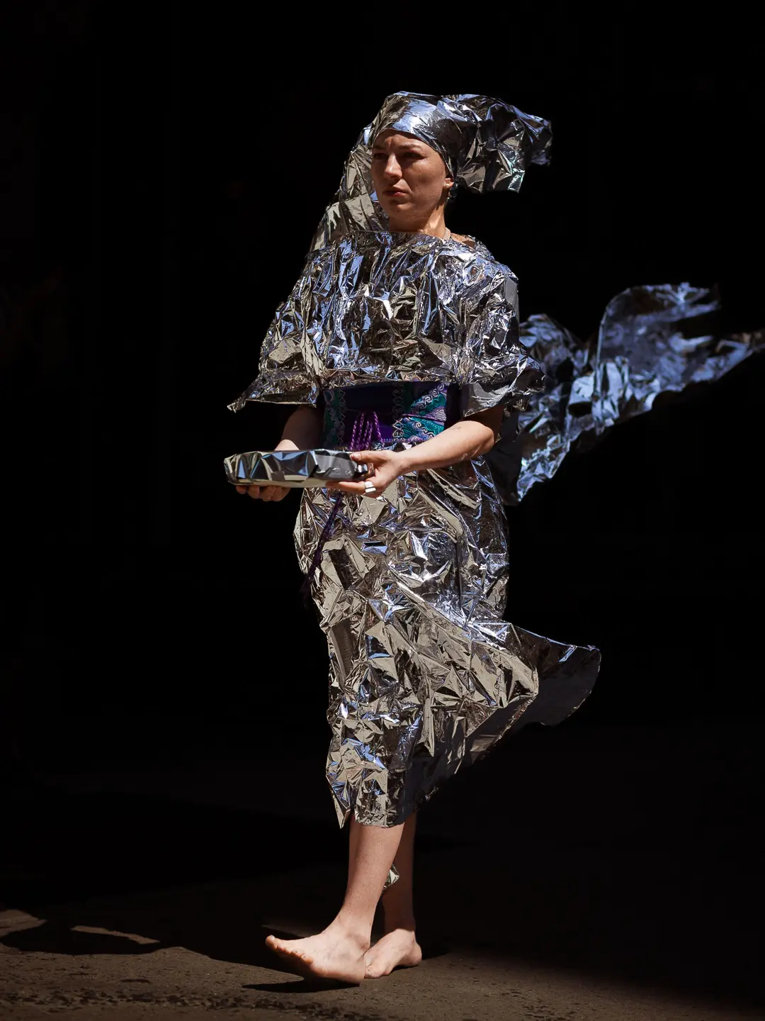Arantxa Araujo, wearing a shiny silver foil, holding a pan, walking on the street.