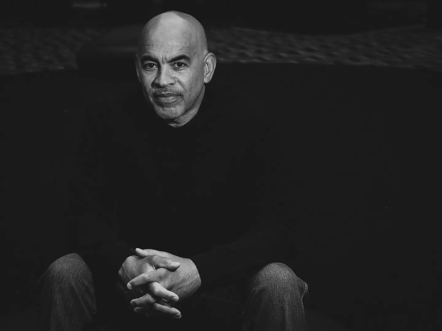 Black-and-white photo of poet Willie Perdomo, sitting with clasped hands against a dark background.
